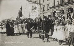 Fane fra  Vålerenga skole med teksten «Vi ere en nation vi med». Foto fra barnetoget på Slottsplassen i Oslo 17. mai 1908. Foto: Nasjonalbiblioteket.